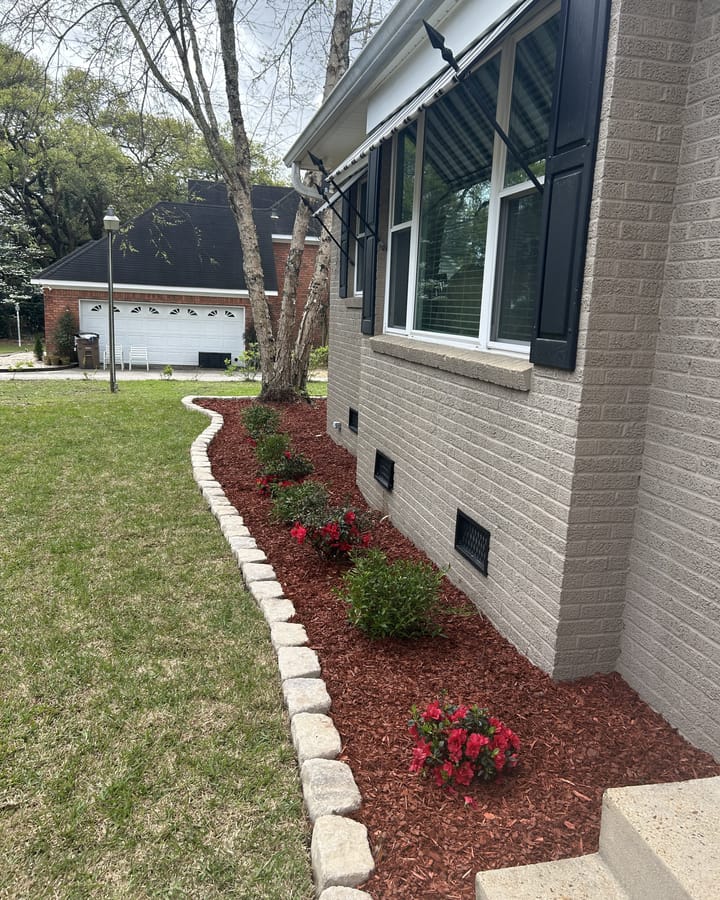 Foundation bed with red mulch, stone edging, and new shrubs beside a brick house