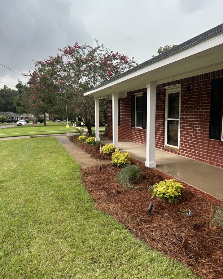 Front porch of a brick house with a new planting bed, pine straw, and fresh sod