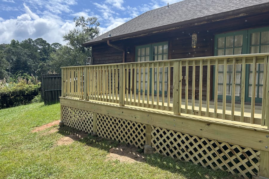 New pressure-treated wood deck with railings and lattice skirting behind a house