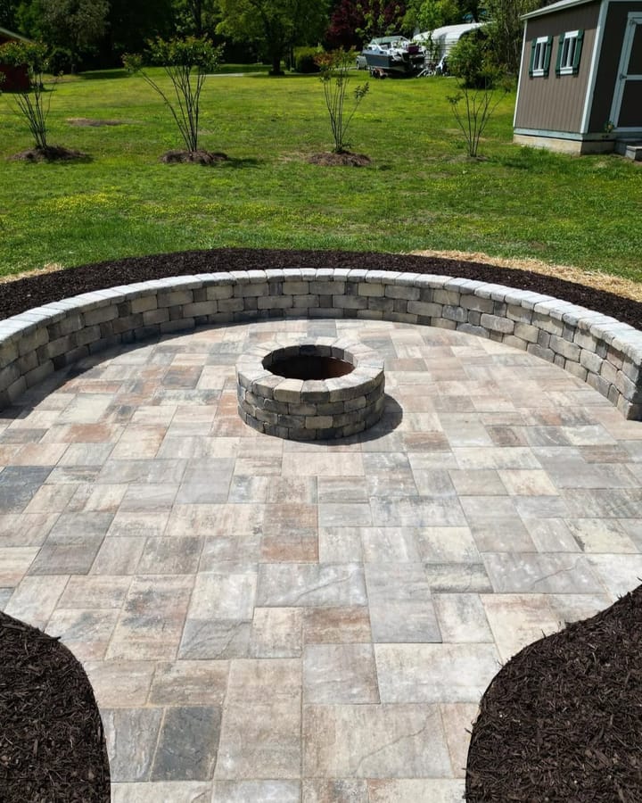 Circular paver patio with a stone fire pit in the centre and a curved block seating wall