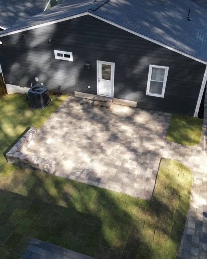 New paver patio behind a dark grey house surrounded by fresh sod