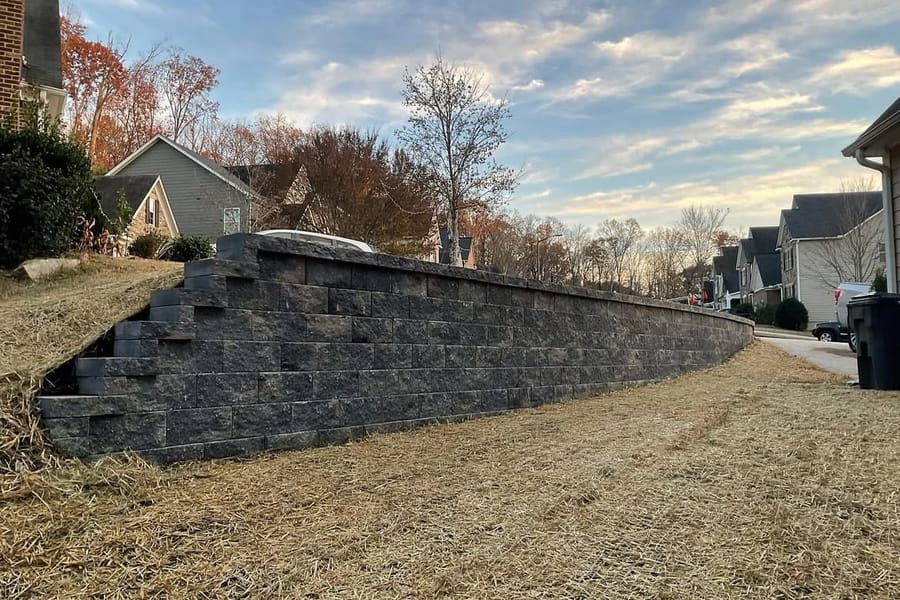 Long segmental block retaining wall along a driveway with a pine-straw slope above it