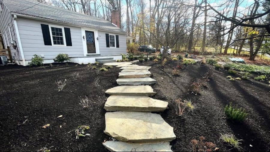 Flagstone stepping-stone path set into a freshly mulched bed in front of a white house