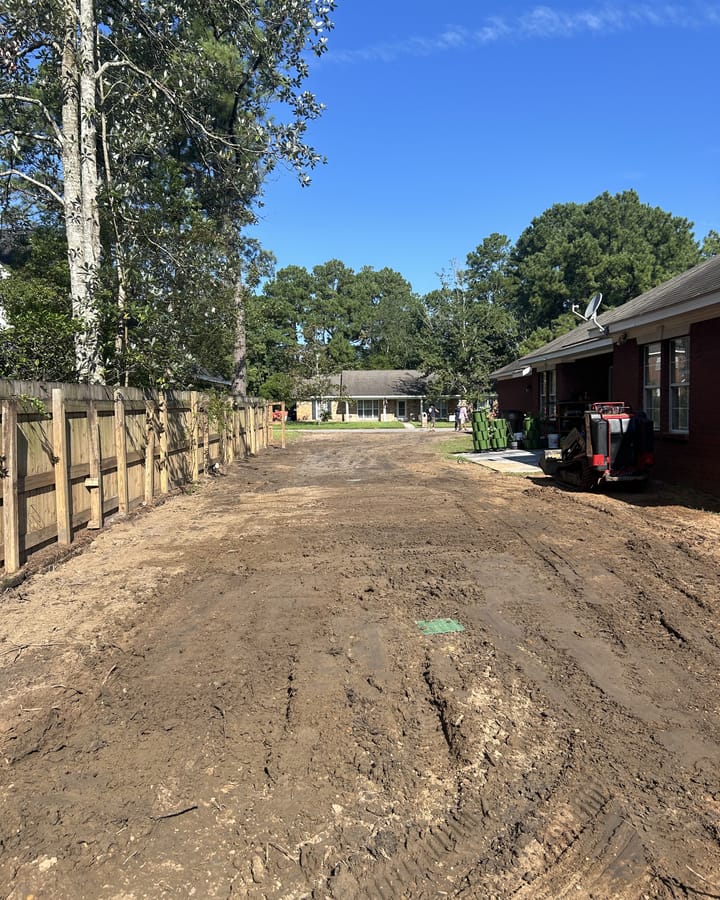 Backyard graded to bare, even soil with a skid steer at the far end and a wood fence along one side